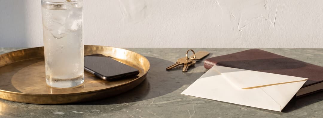 Il tavolo di lavoro di un concierge nel pomeriggio, un vassoio di ottone e un bicchiere d'acqua di king coconut accanto a un registro del giorno chiuso