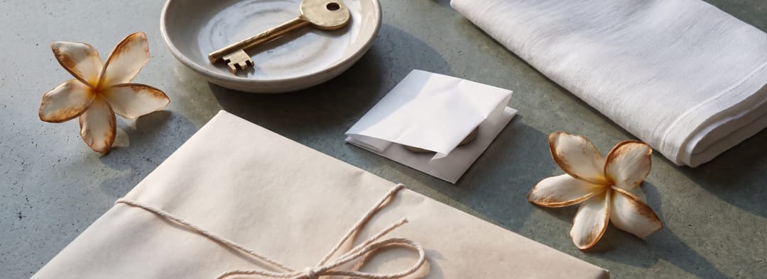 Un pacco avvolto, una chiave di ottone restituita in un piatto di ceramica e frangipani di un giorno oltre il loro momento migliore, sotto una luce d'argento