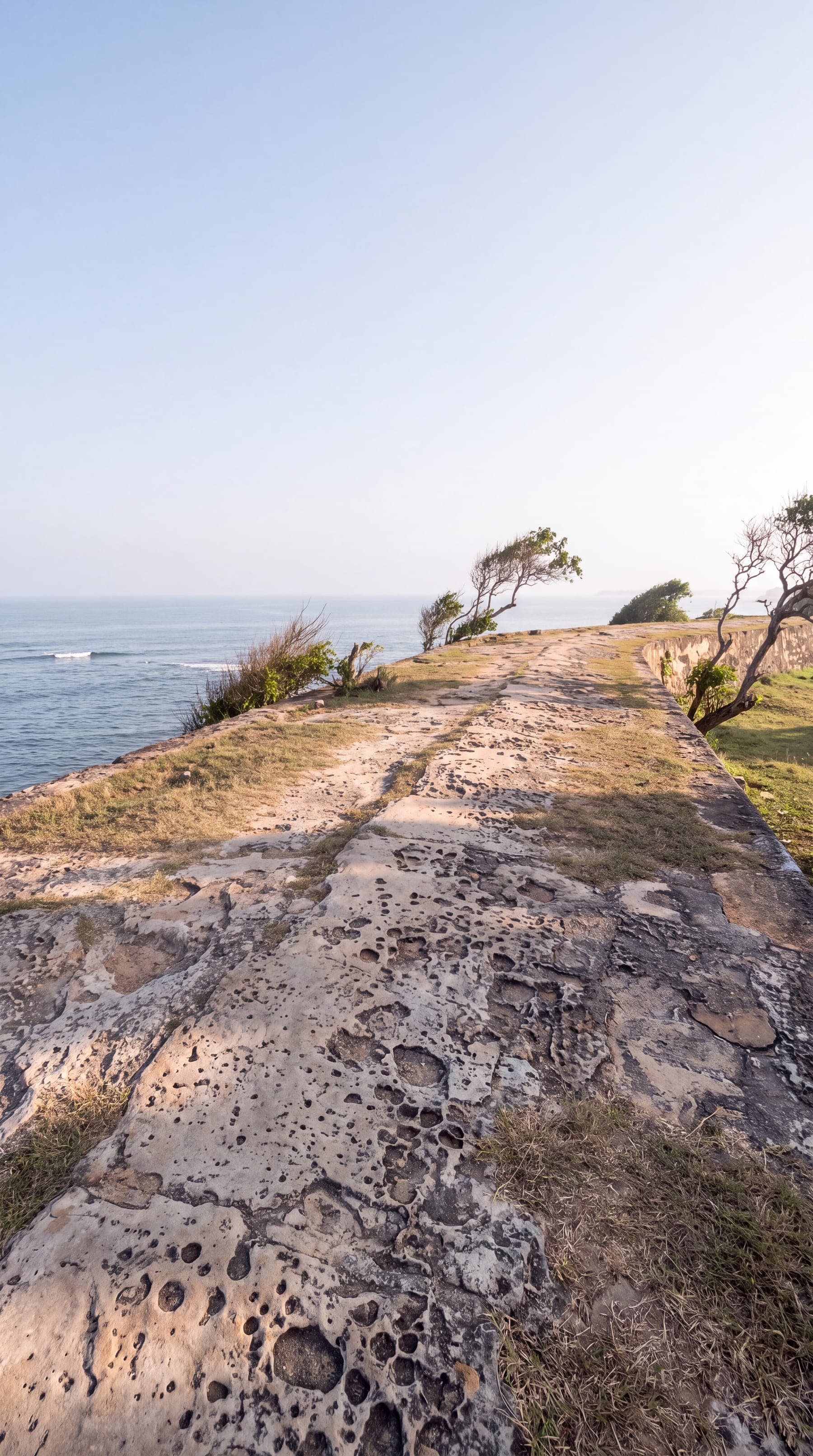 The grassed rampart of Galle Fort above the sea, a stone path and wind-bent trees