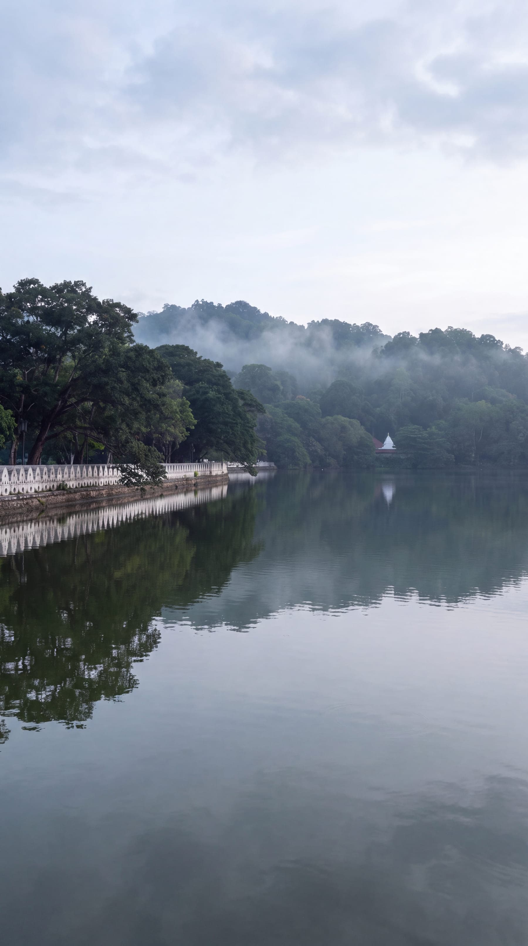 Kandy Lake at dawn, the white cloud wall along its edge and the hills reflected