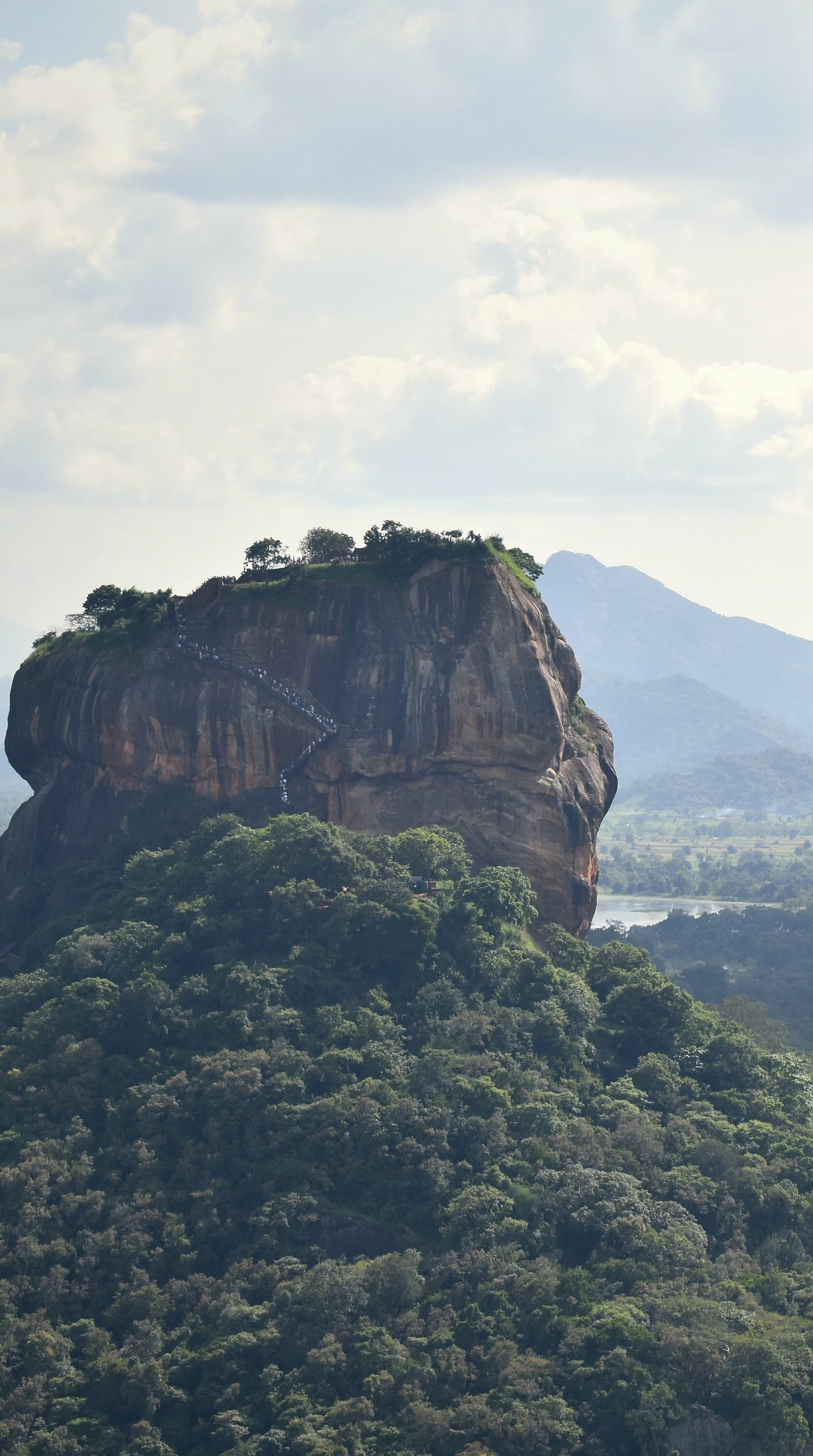The Sigiriya rock rising from the forest, seen from Pidurangala, with blue hills behind
